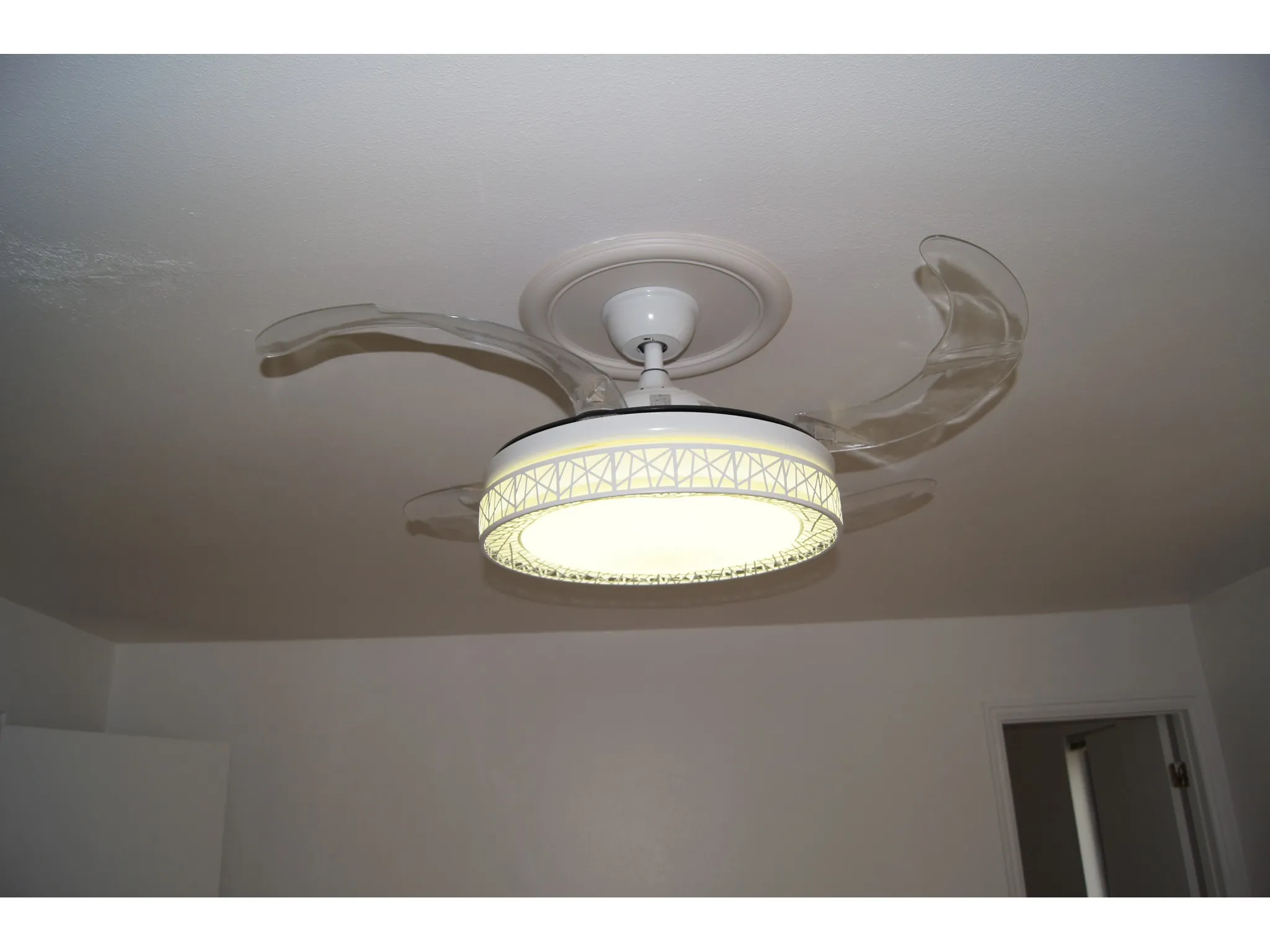 Master Bedroom Ceiling-mounted fixture featuring retractable clear fan blades and an integrated circular light with a decorative geometric pattern