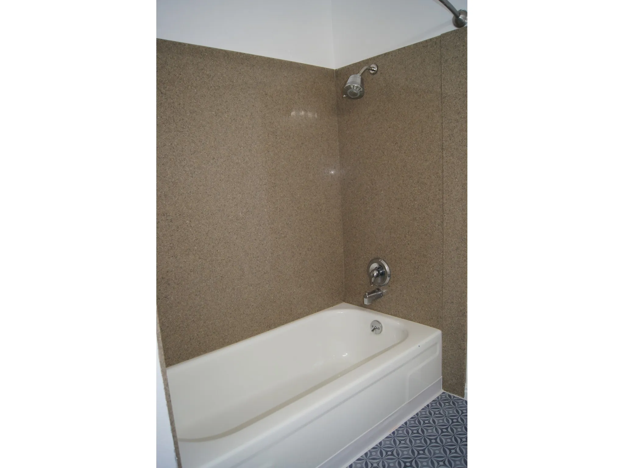 Tub and shower combination featuring speckled brown wall surrounds and a white porcelain tub