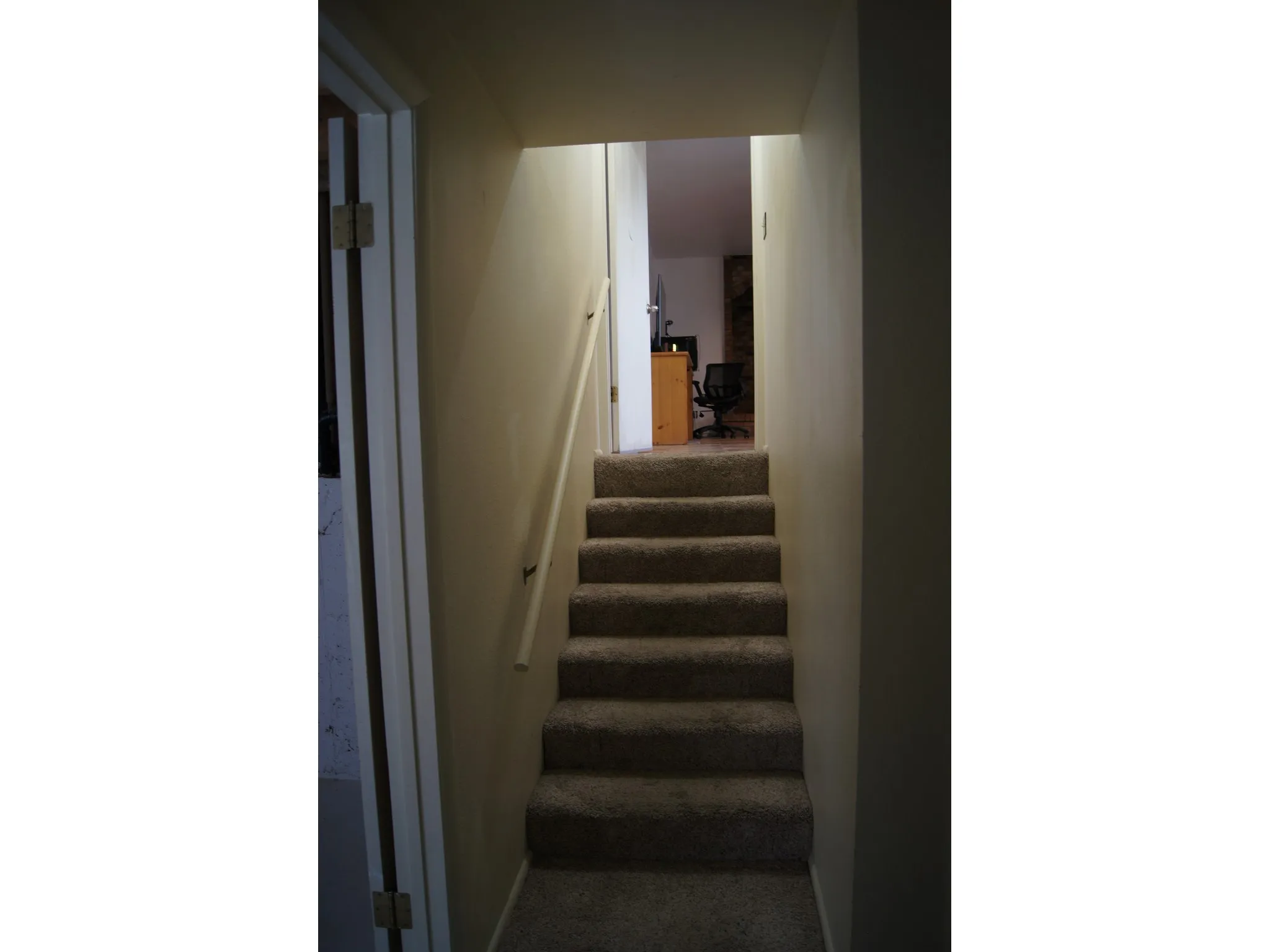 Carpeted staircase with a white wall-mounted handrail and light beige wall paint