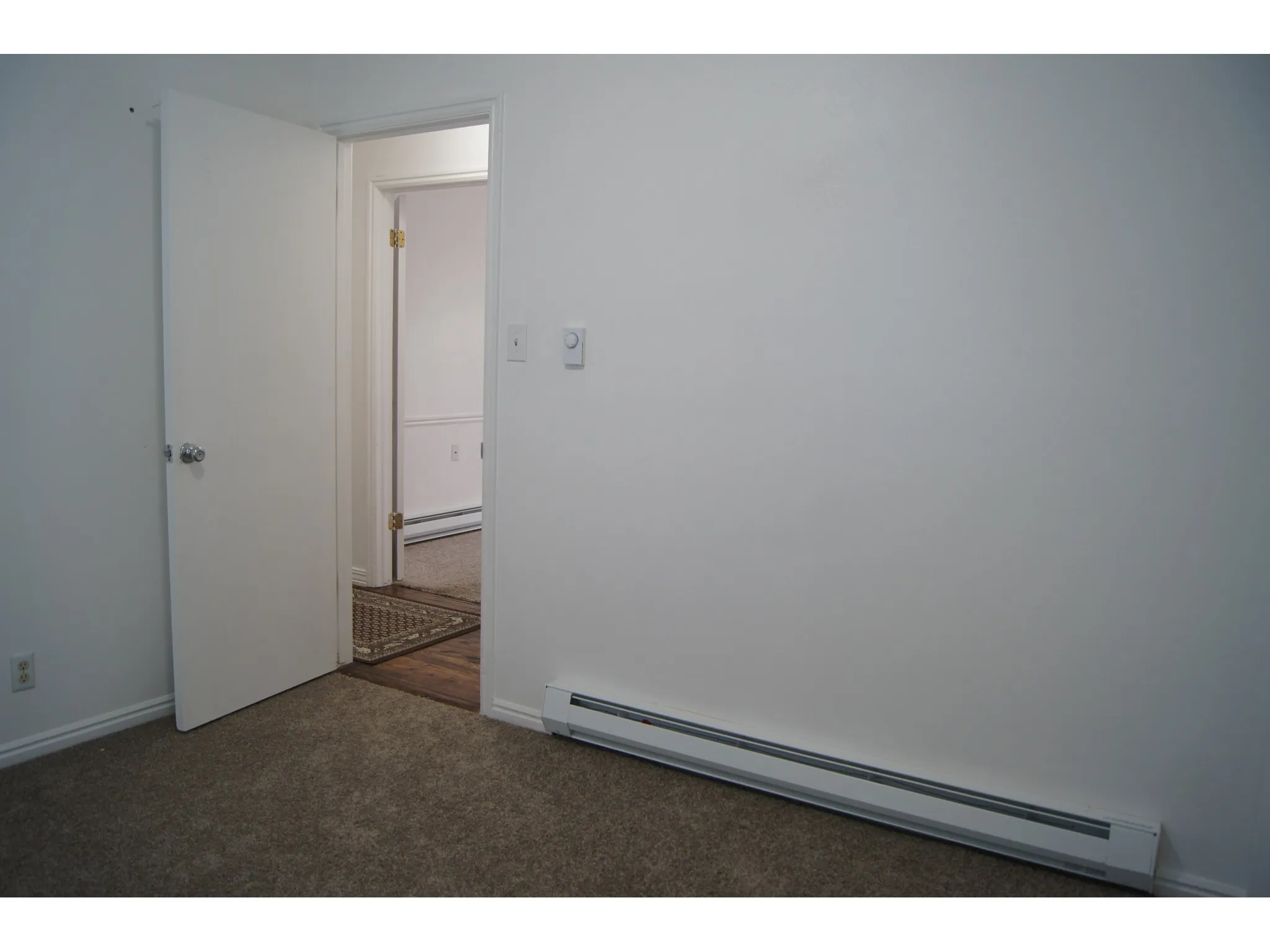 Bedroom 2 Carpeted interior space featuring a white door with chrome hardware, white baseboards, and a baseboard heater