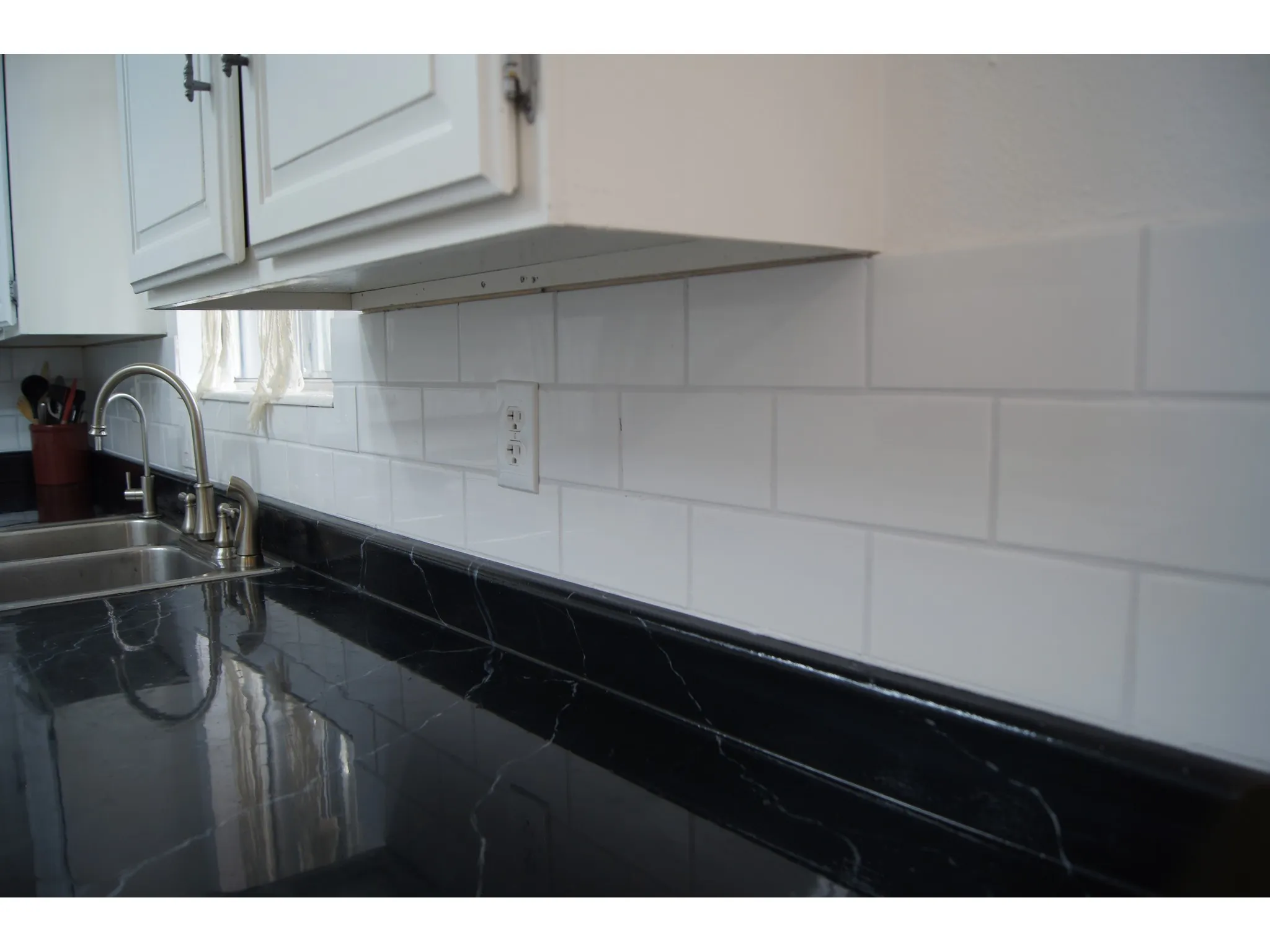 Kitchen area featuring a stainless steel double-basin sink with a gooseneck faucet, white subway tile backsplash, and dark countertops with light veining
