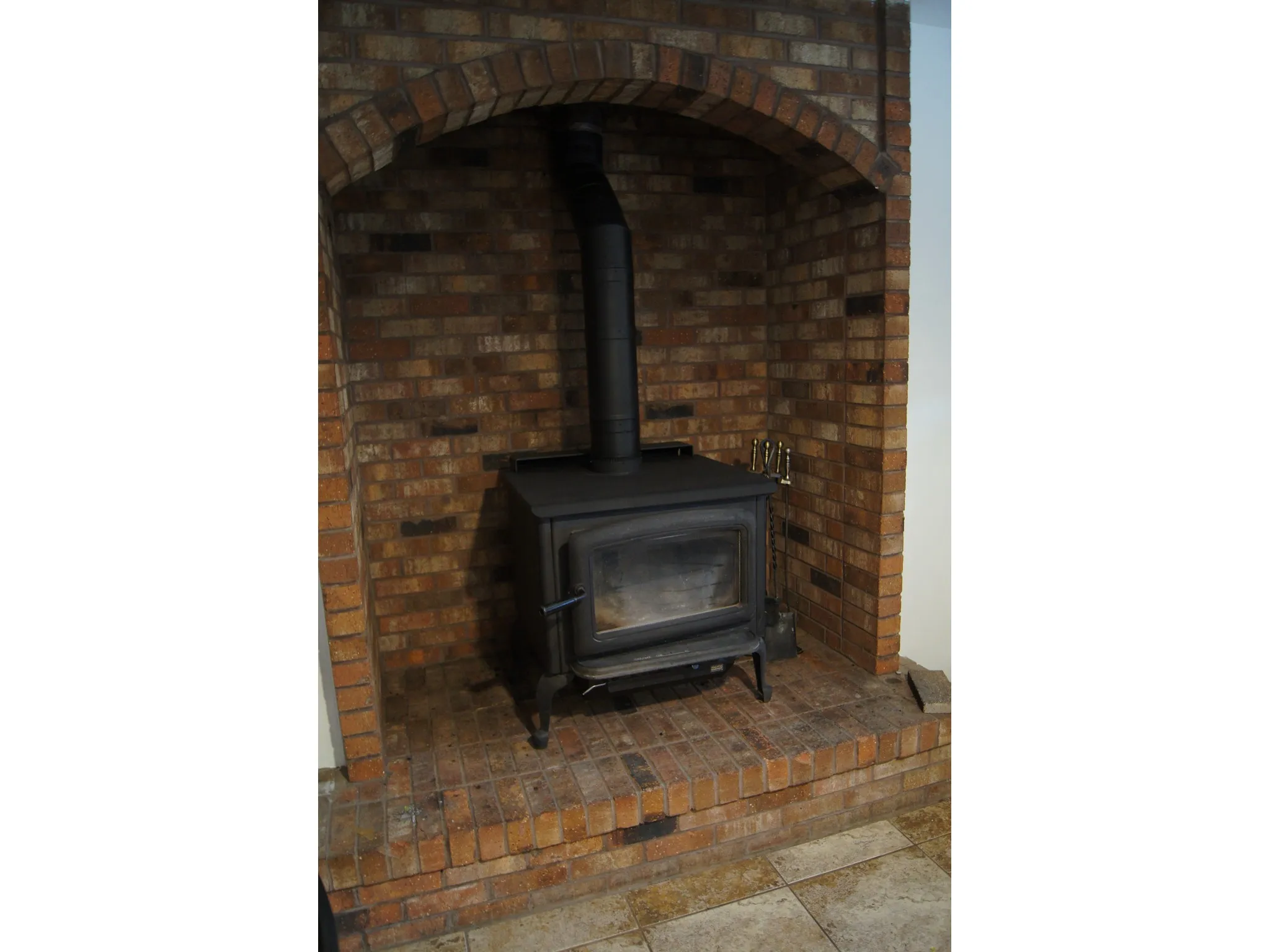 Brick fireplace with an arched opening, featuring a black wood-burning stove and a brick hearth