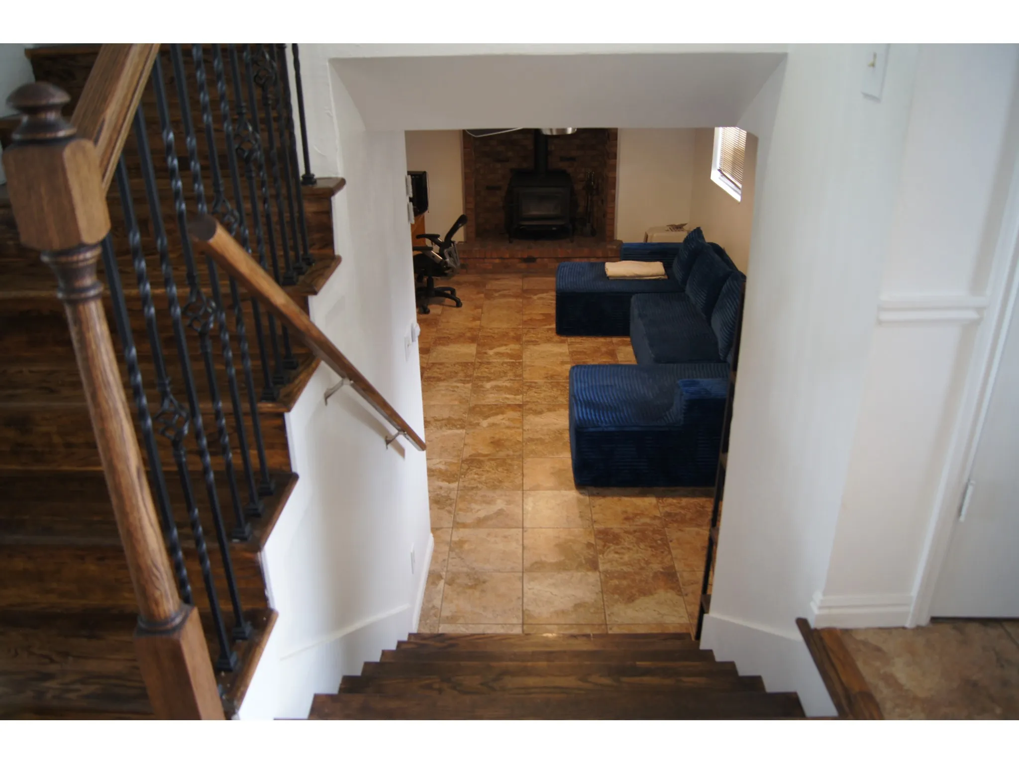 Wood-finish stairs with wrought iron balusters leading to a tiled lower level