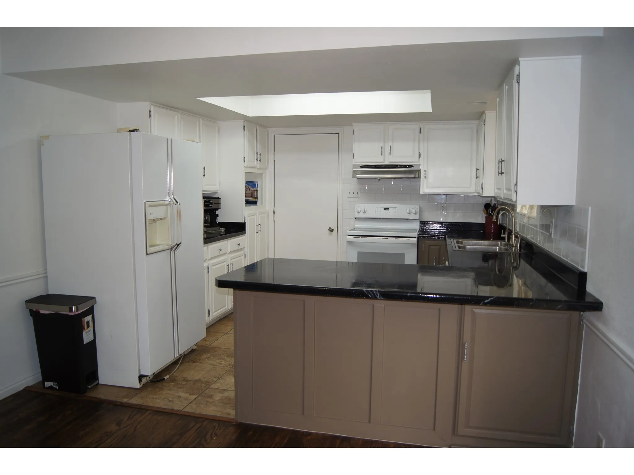 Kitchen featuring white cabinetry, dark countertops, a white appliance suite, a central island with paneling, and a skylight