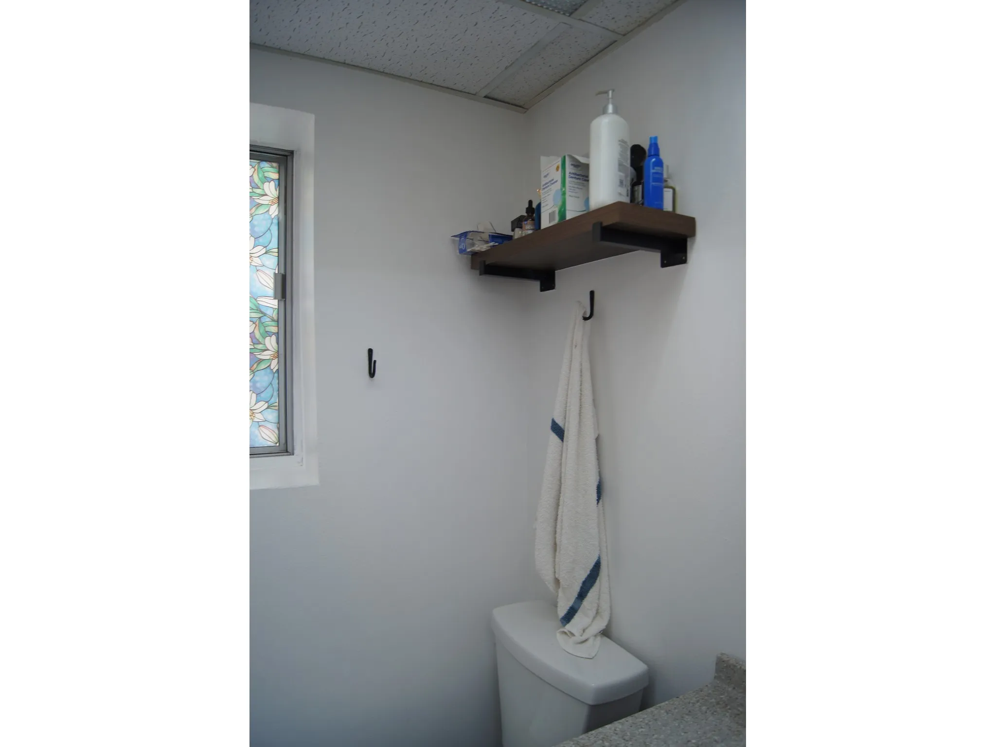Bathroom featuring a stained-glass window, a wood-finish floating shelf with black brackets, and a light-toned countertop