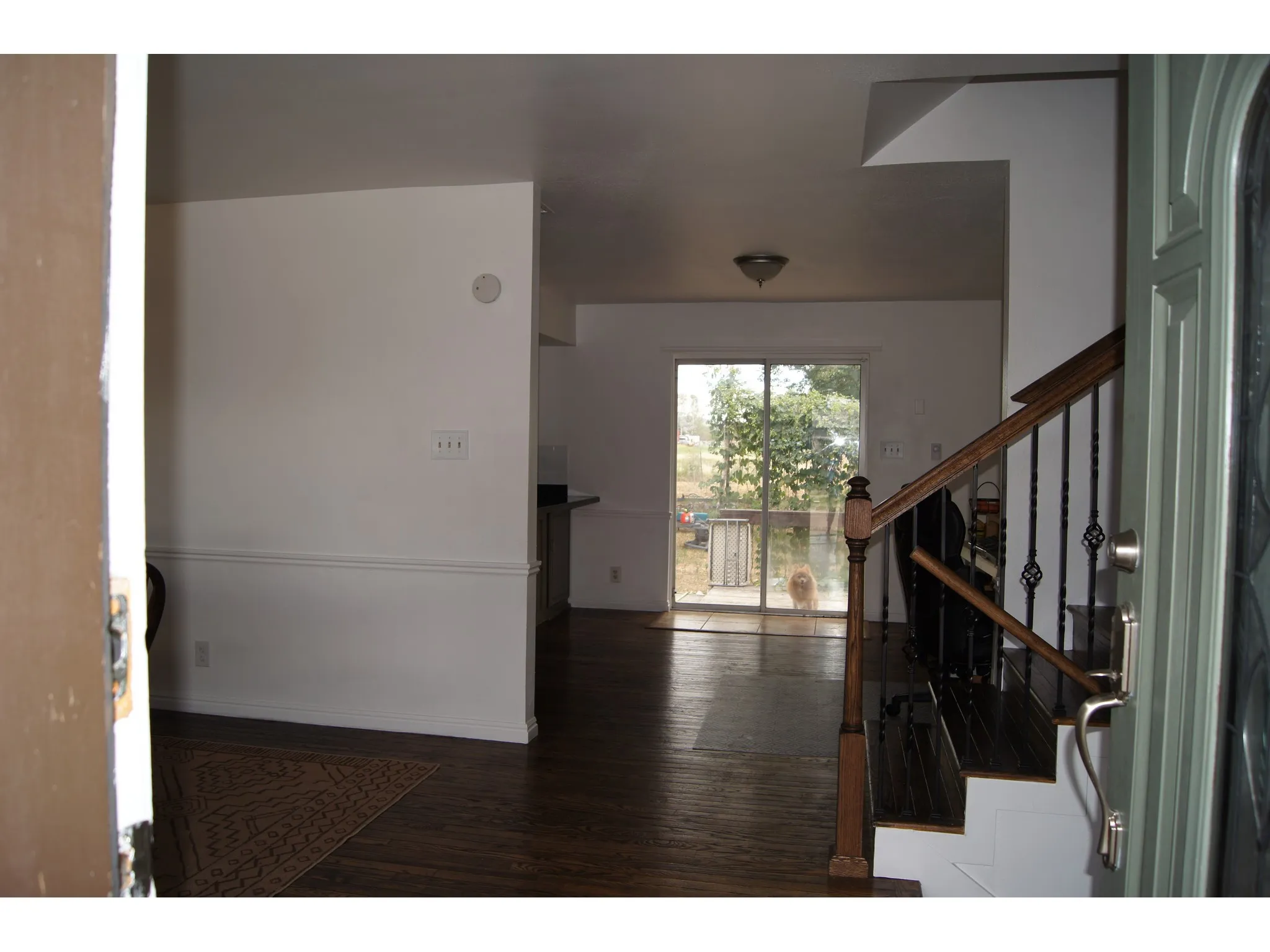 Entryway featuring wood-finish flooring, a staircase with dark wood banister and wrought iron spindles, white baseboards, and chair rail molding