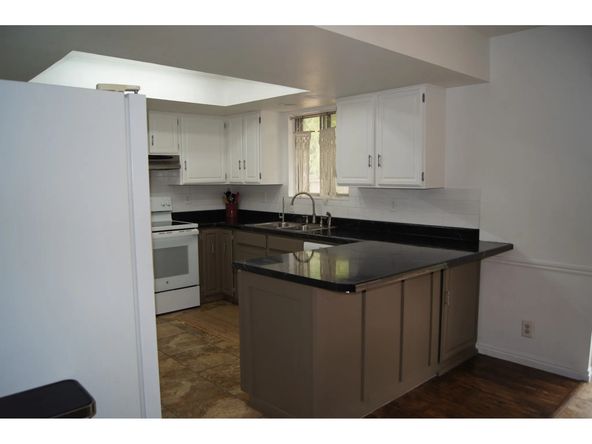 Kitchen featuring white upper cabinetry, dark countertops, a tile backsplash, and a built-in breakfast bar
