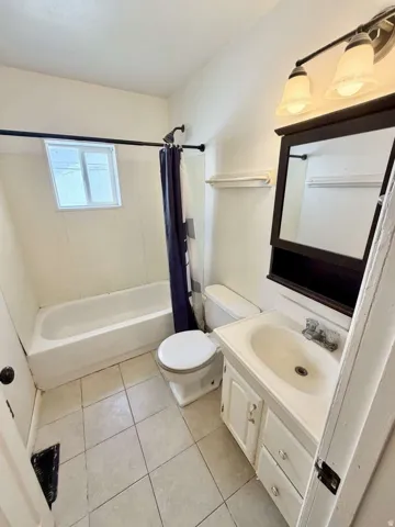 Bathroom featuring square tile flooring, a white porcelain bathtub with a shower fixture, a white toilet, and a vanity with a white basin sink and cabinet storage