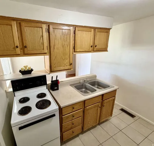 Kitchen featuring wood-finish cabinetry, a double basin stainless steel sink, and a white electric range