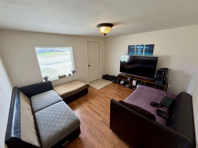 Living area featuring wood-finish flooring, a white paneled entry door, and a single window with a white frame