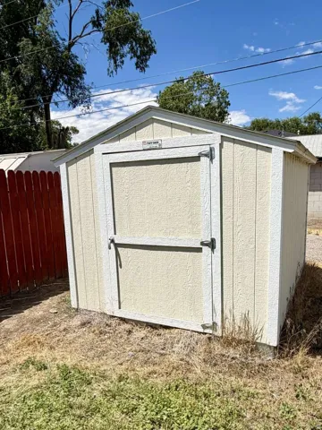 Outdoor storage shed featuring a gable roof, light-colored siding, and a single door with a dark handle