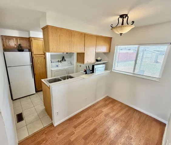 Kitchen area featuring light wood cabinetry, a double basin stainless steel sink, and a white refrigerator
