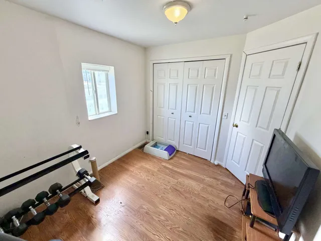Room featuring wood-finish flooring, a window with blinds, a ceiling-mounted light fixture, a paneled bifold closet door, and a paneled entry door
