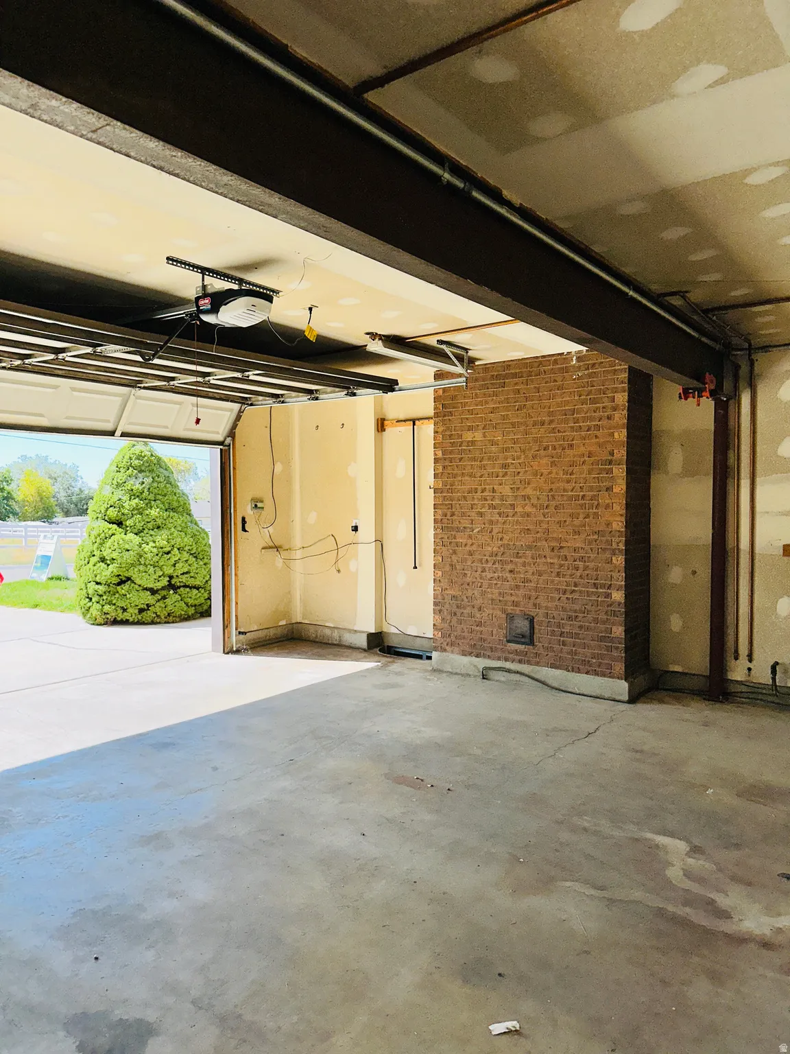 Attached garage with exposed brick wall, concrete flooring, and an overhead garage door opener