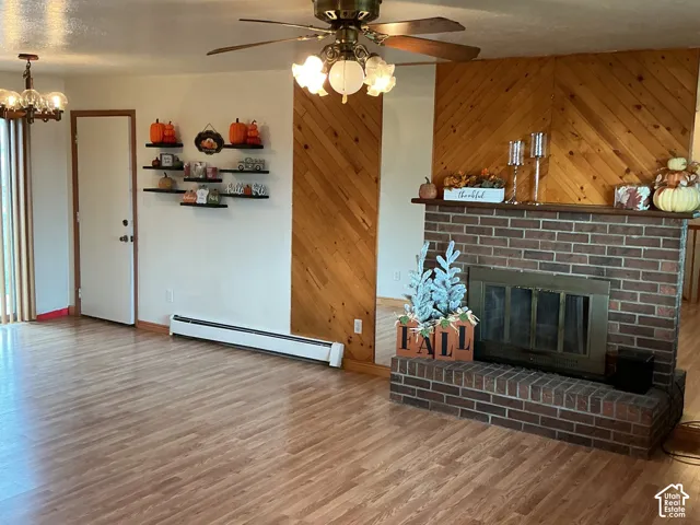 Brick fireplace with a raised hearth, diagonal wood-paneling accent wall, wood-finish flooring, and multi-light ceiling fan