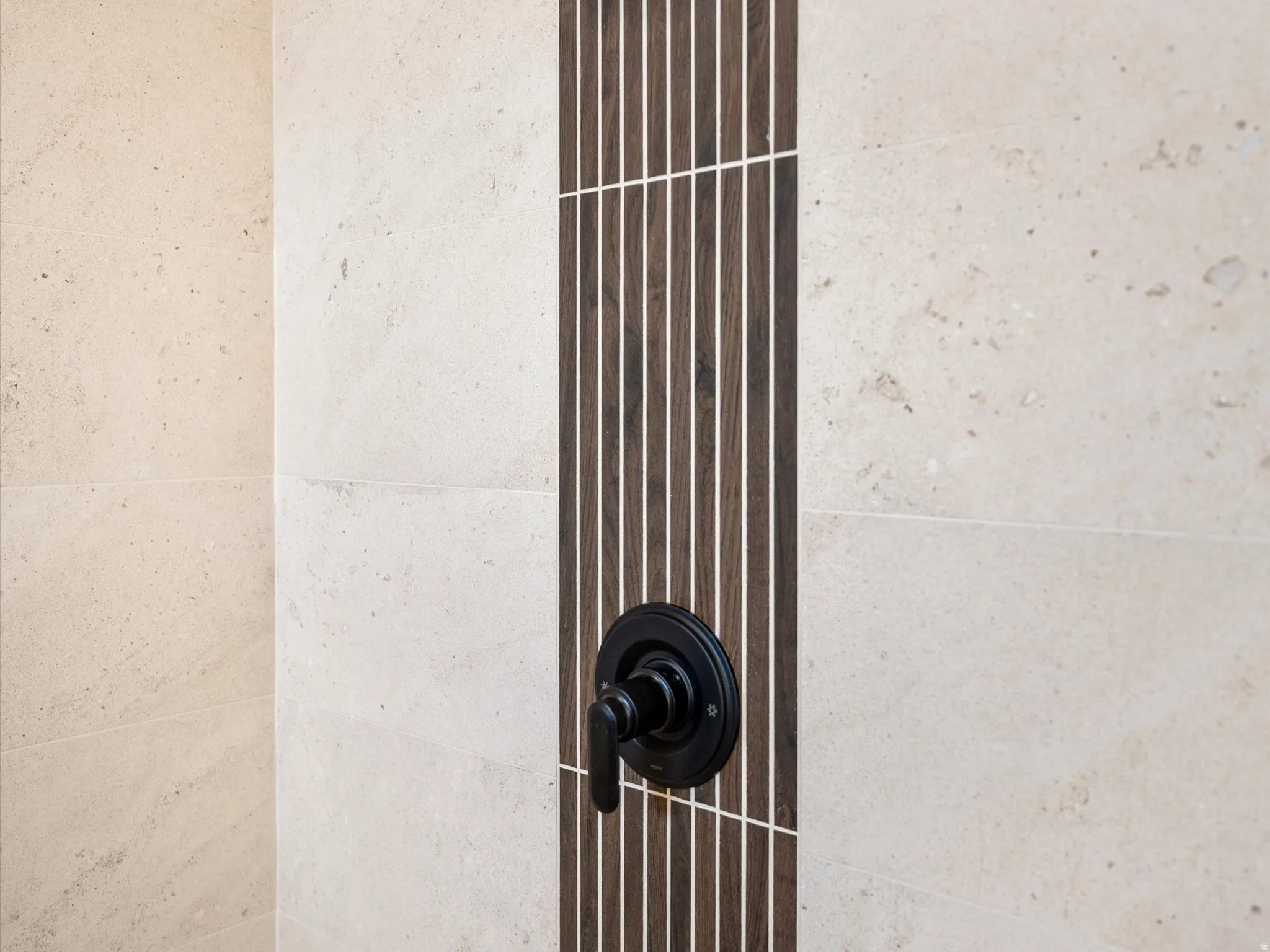 Shower wall featuring large format light-toned tile with a vertical accent strip of thin, dark wood-finish tiles