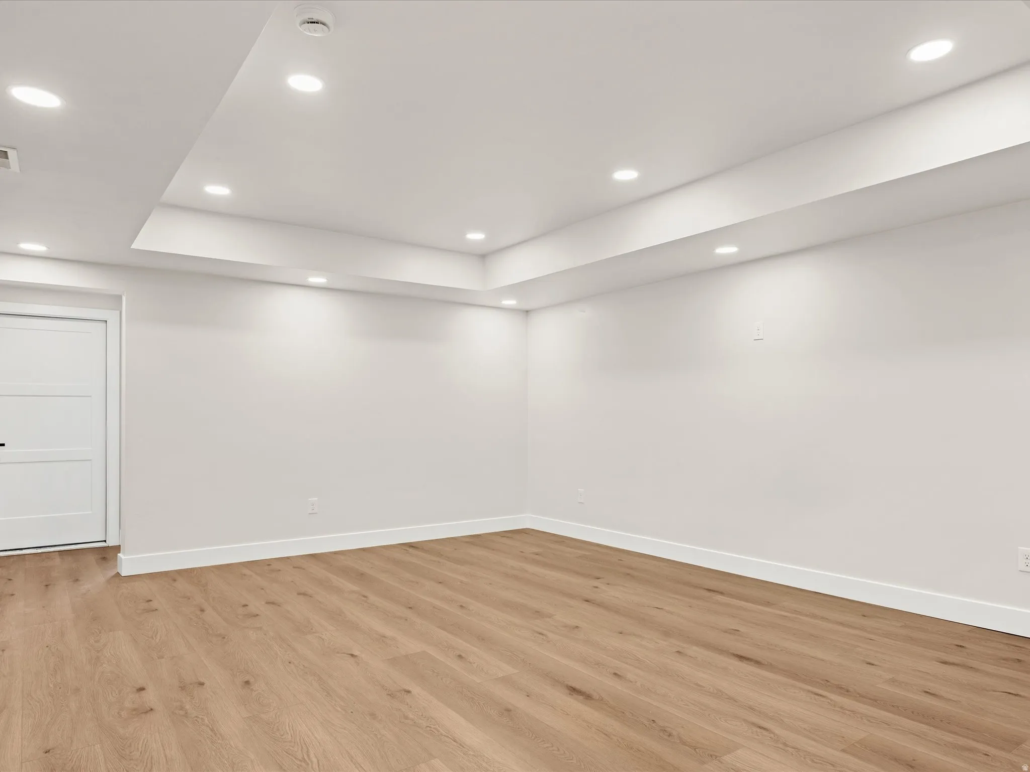 Bright interior space featuring light wood-finish flooring, white walls, and a multi-level ceiling with recessed lighting