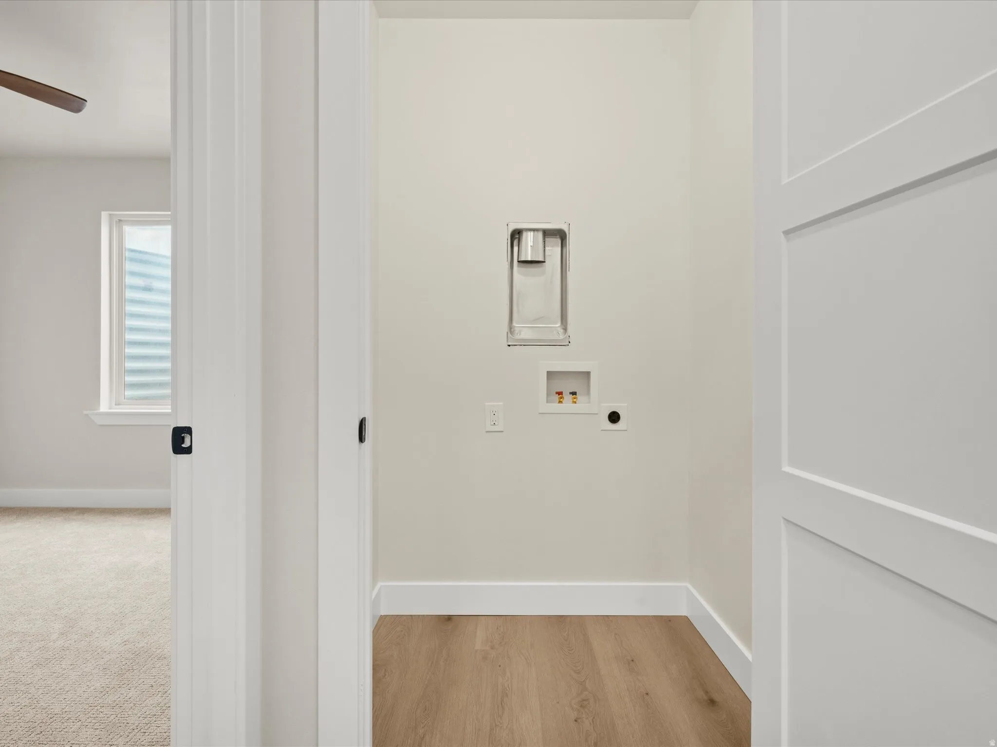 Dedicated laundry alcove featuring light wood-finish flooring, white baseboards, and neutral wall paint