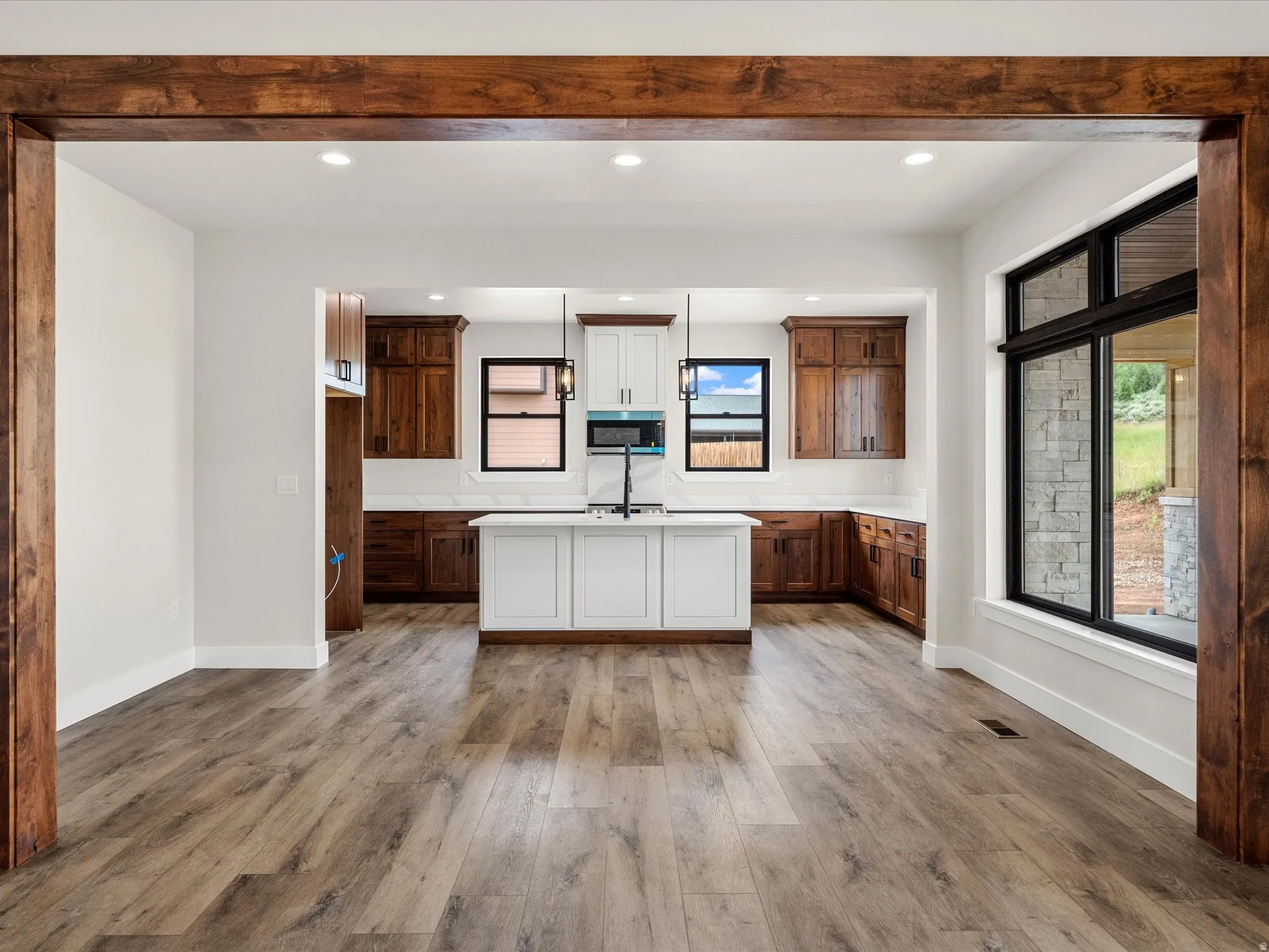 Expansive kitchen featuring a central island with integrated sink, recessed lighting, wood-finish flooring, two-tone cabinetry, and a large window with black framing
