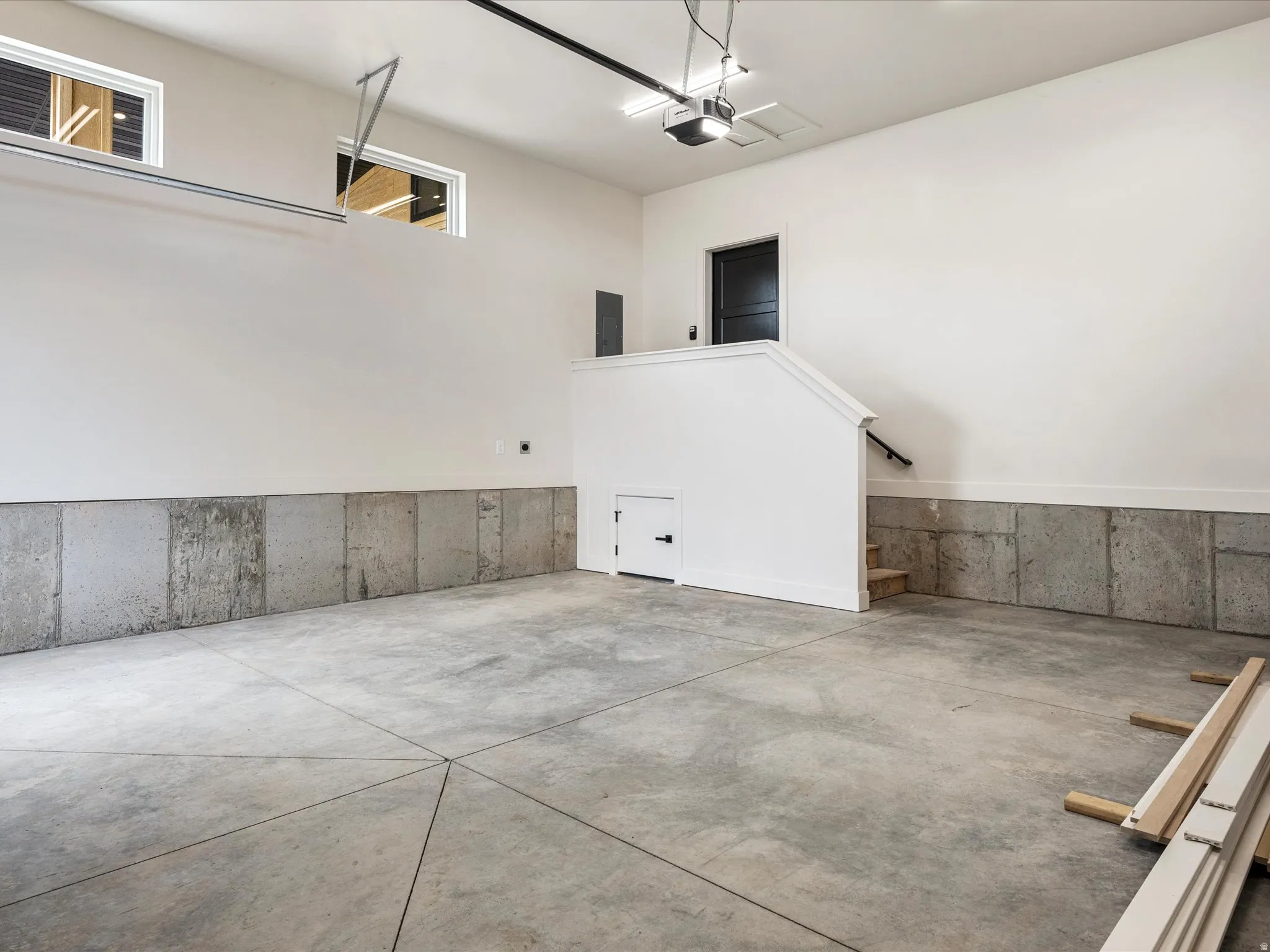 Spacious garage featuring a concrete floor with geometric scoring, concrete wainscoting, and high transom windows