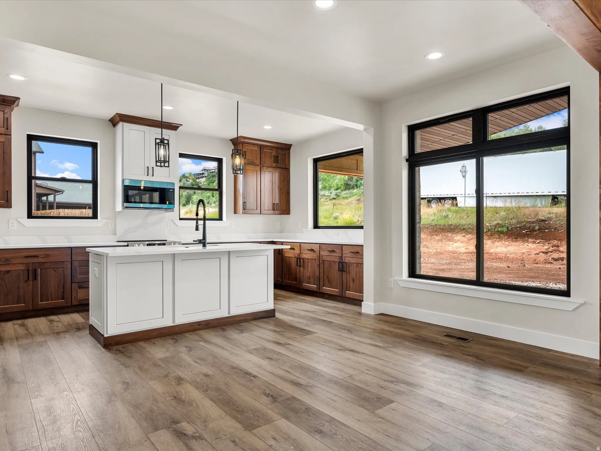 Spacious kitchen featuring a central island with paneling, wood-finish flooring, two-tone cabinetry, white countertops, and expansive windows with black framing