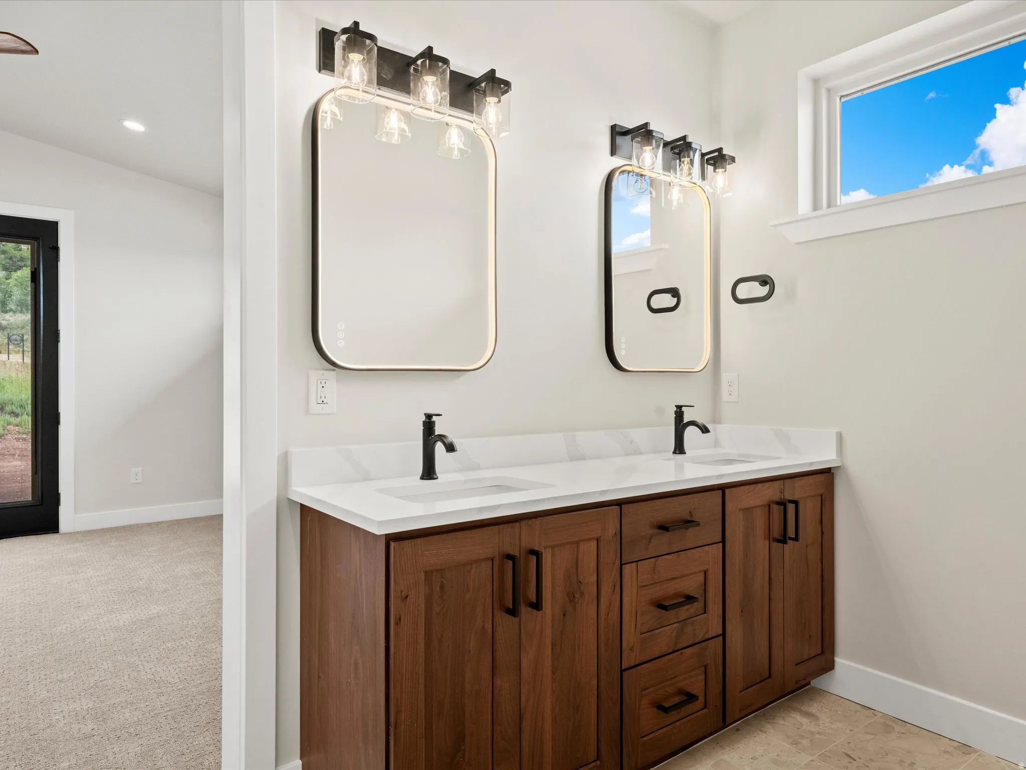 Dual vanity featuring wood-finish cabinetry, white countertops, and matte black fixtures