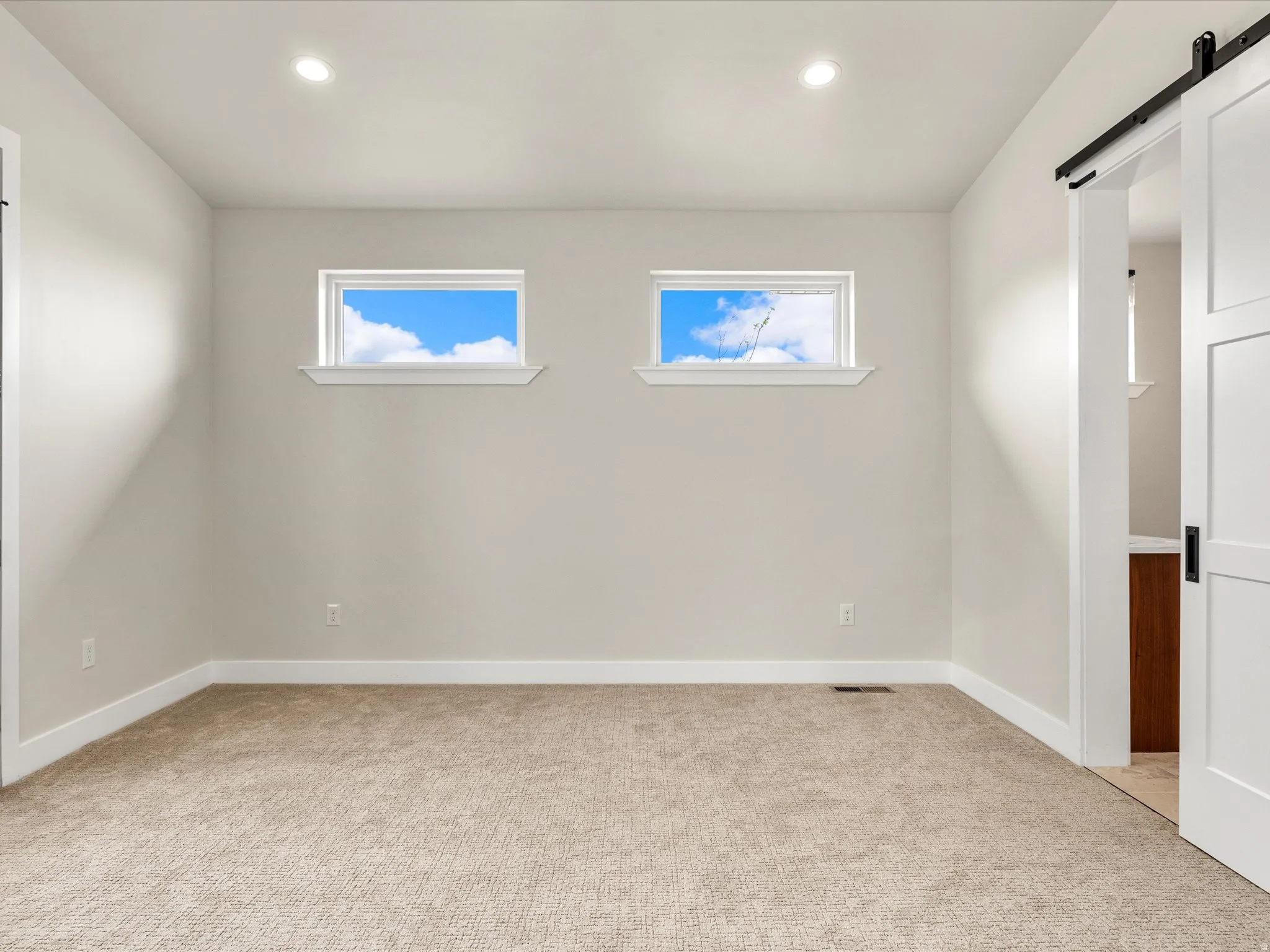 Neutral-toned room featuring two transom windows, recessed ceiling lighting, and beige carpet flooring