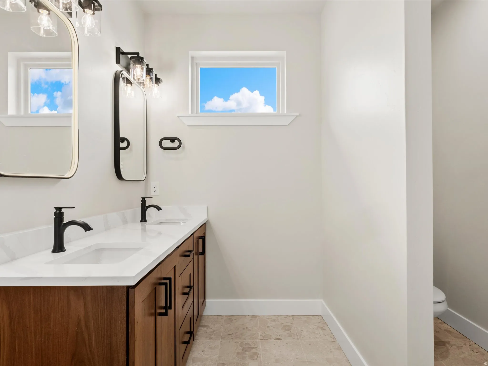 Bathroom featuring a dual vanity with wood-finish cabinetry, white countertop, and matte black fixtures