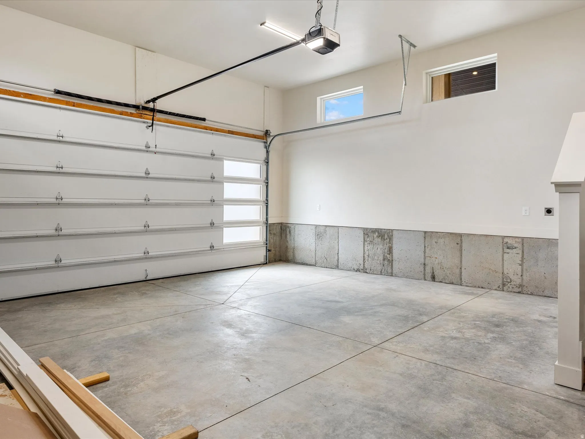 Spacious garage featuring a concrete floor, overhead door with frosted glass panels, automatic garage door opener, and two high-set windows