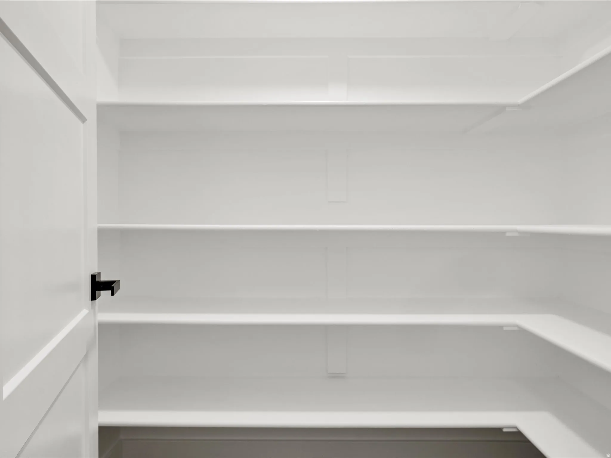 Pantry with multiple white shelves, a white interior, and a white door with a black handle
