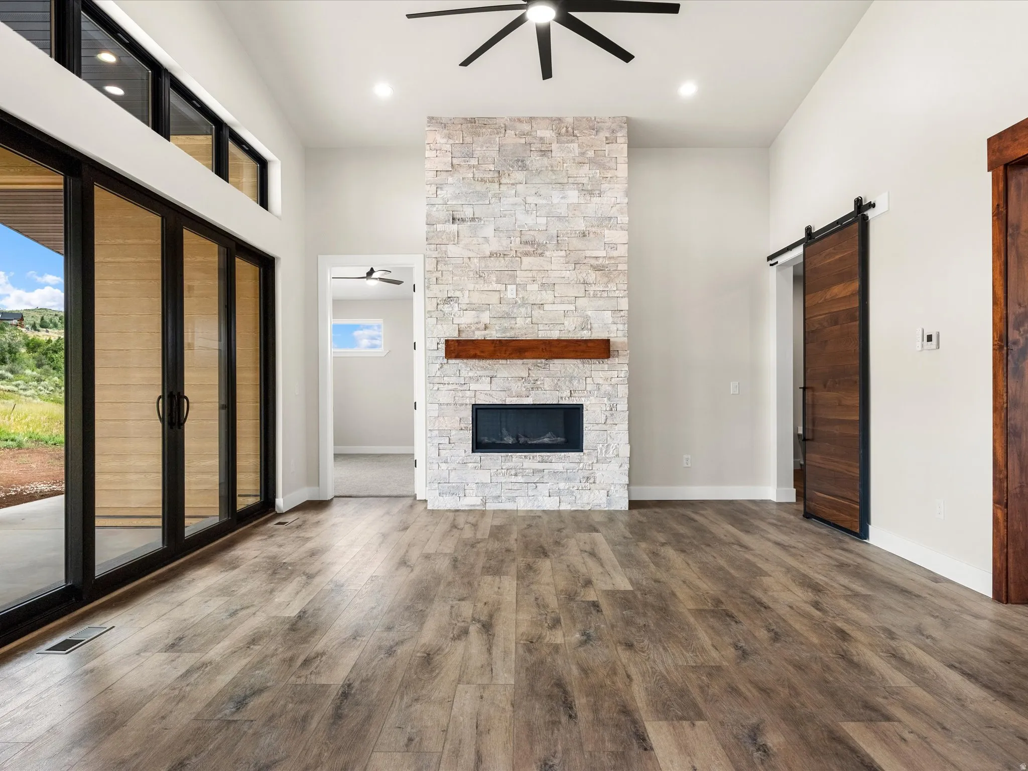 Spacious room featuring wood-finish flooring, a stacked stone fireplace with a wood mantel, and a dark wood barn door