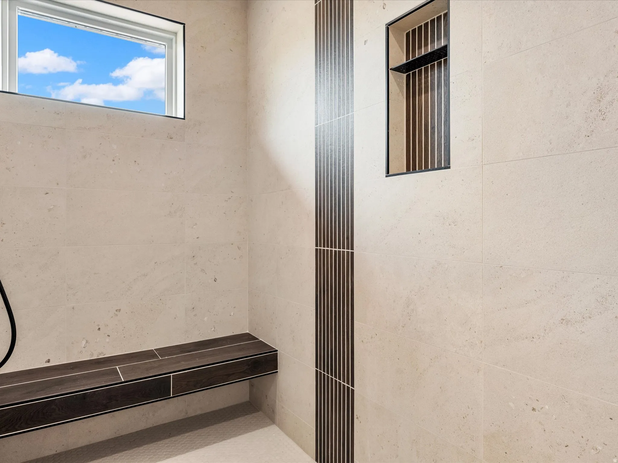 Shower enclosure featuring light-toned large format wall tiles, a built-in dark wood-finish bench, and a rectangular window