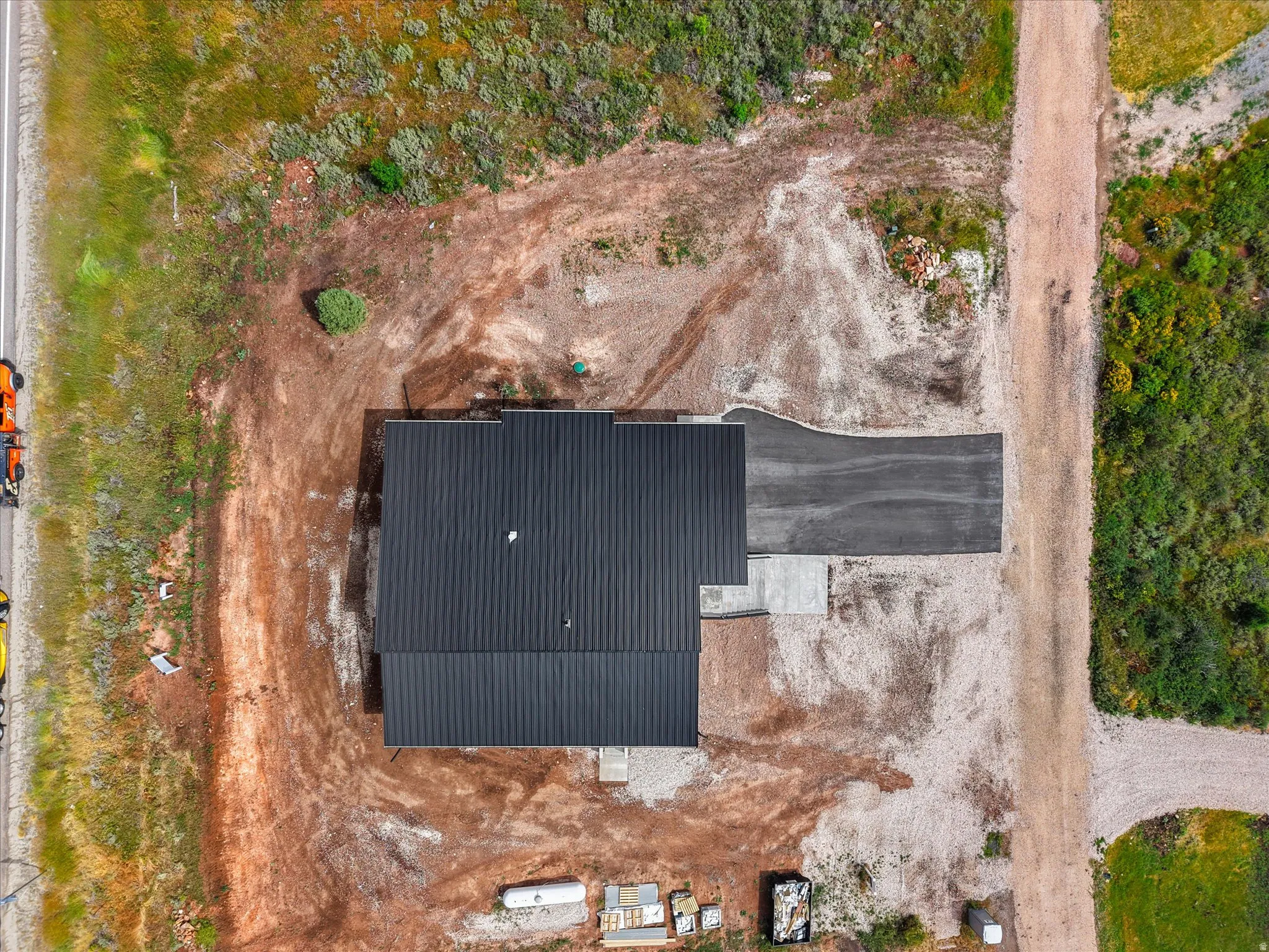 New construction with a dark metal roof, featuring a paved driveway and an adjacent gravel road