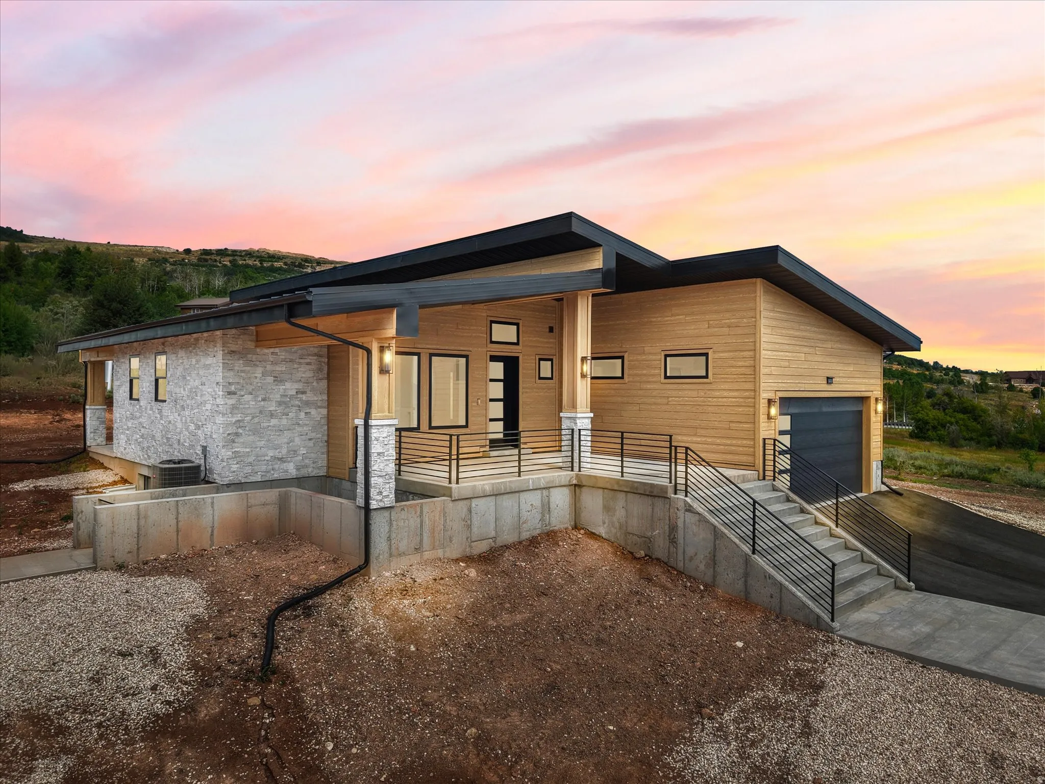 Modern architectural exterior featuring wood-finish siding, stone accents, a multi-pane front door, and a black garage door