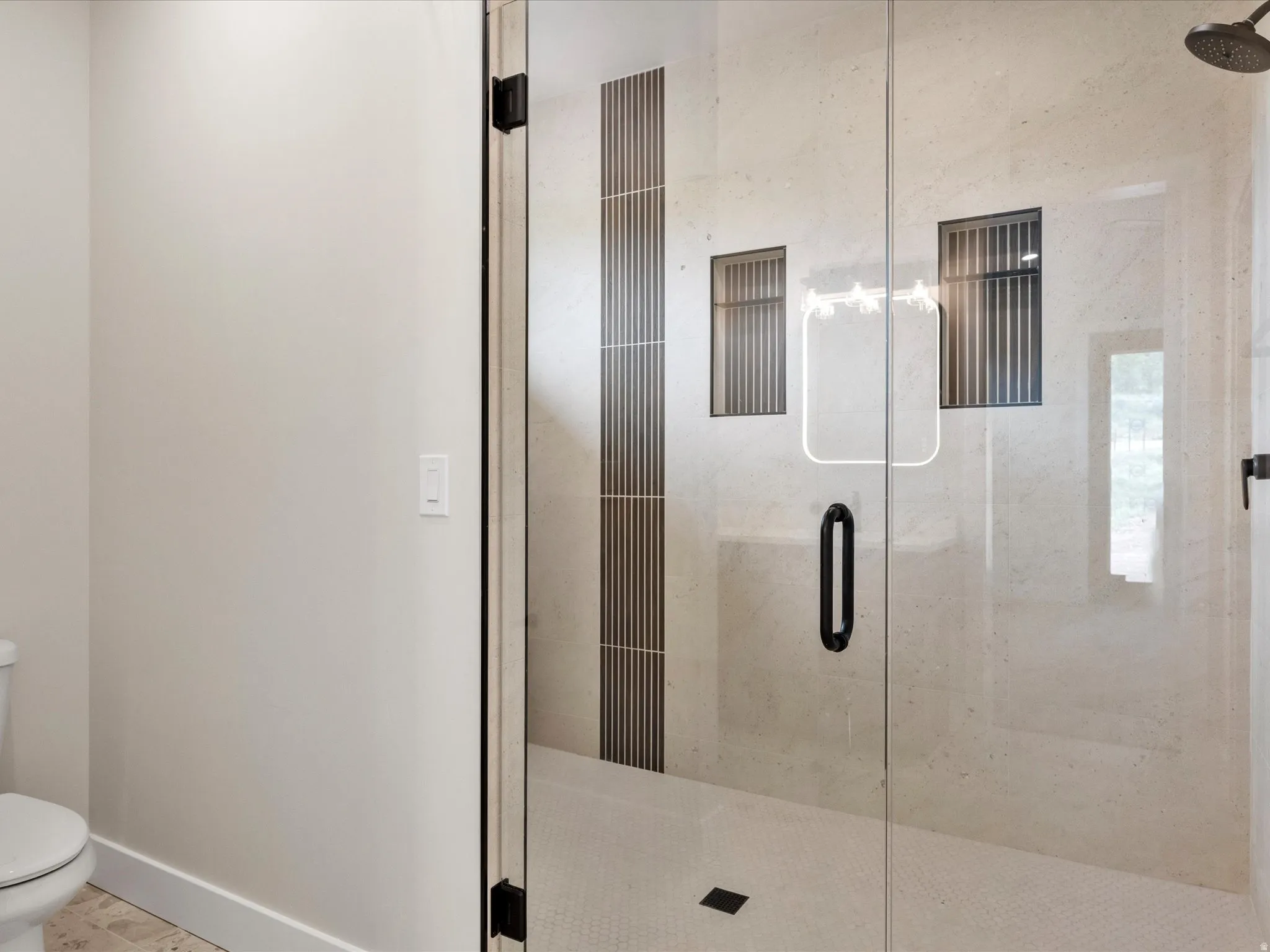 Glass-enclosed shower featuring a dark bronze rainfall showerhead, integrated tiled niches, and a textured vertical accent tile band