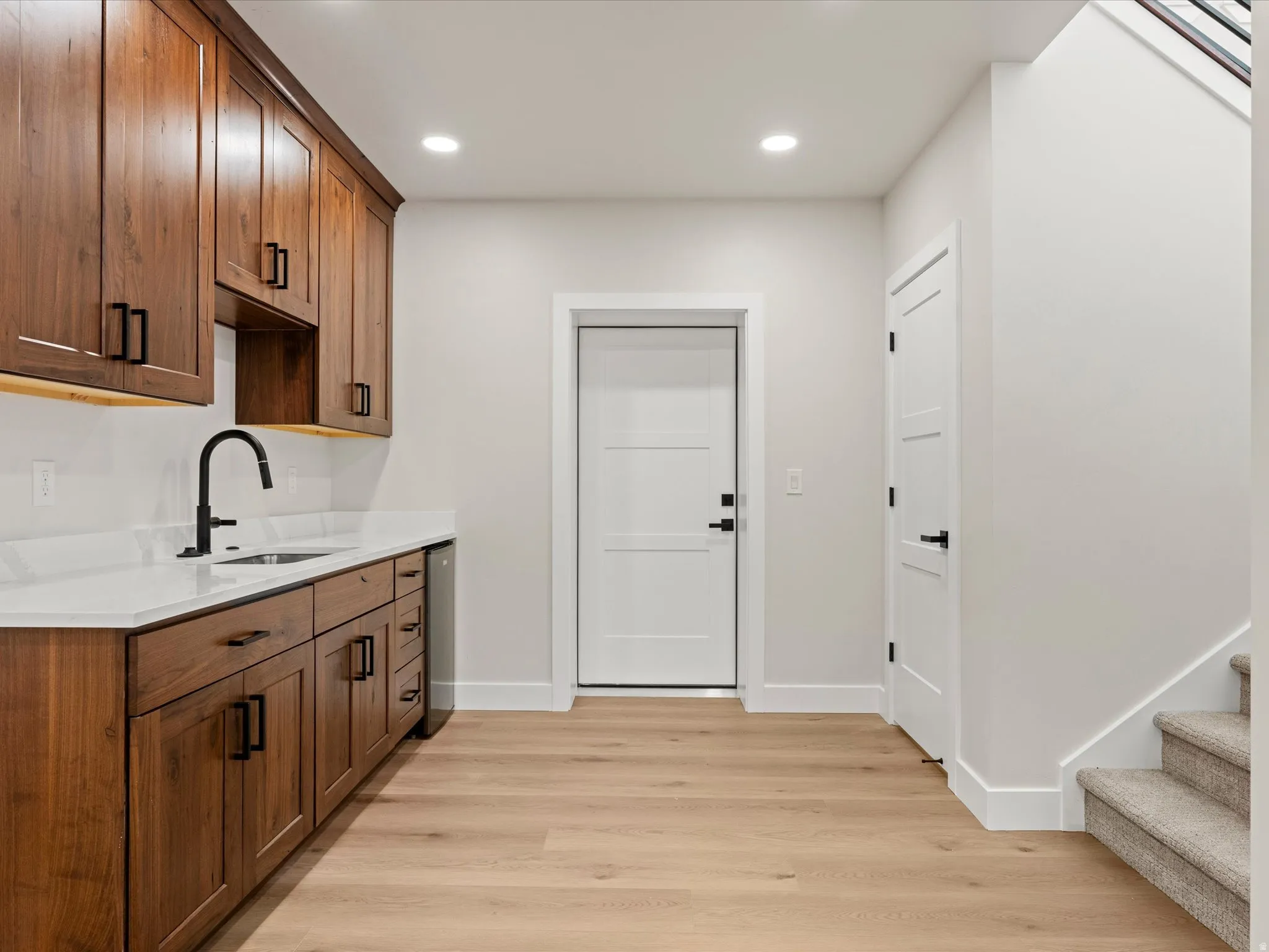 Wet bar featuring wood cabinetry with matte black hardware, white countertop, undermount sink with a gooseneck faucet, and integrated beverage cooler