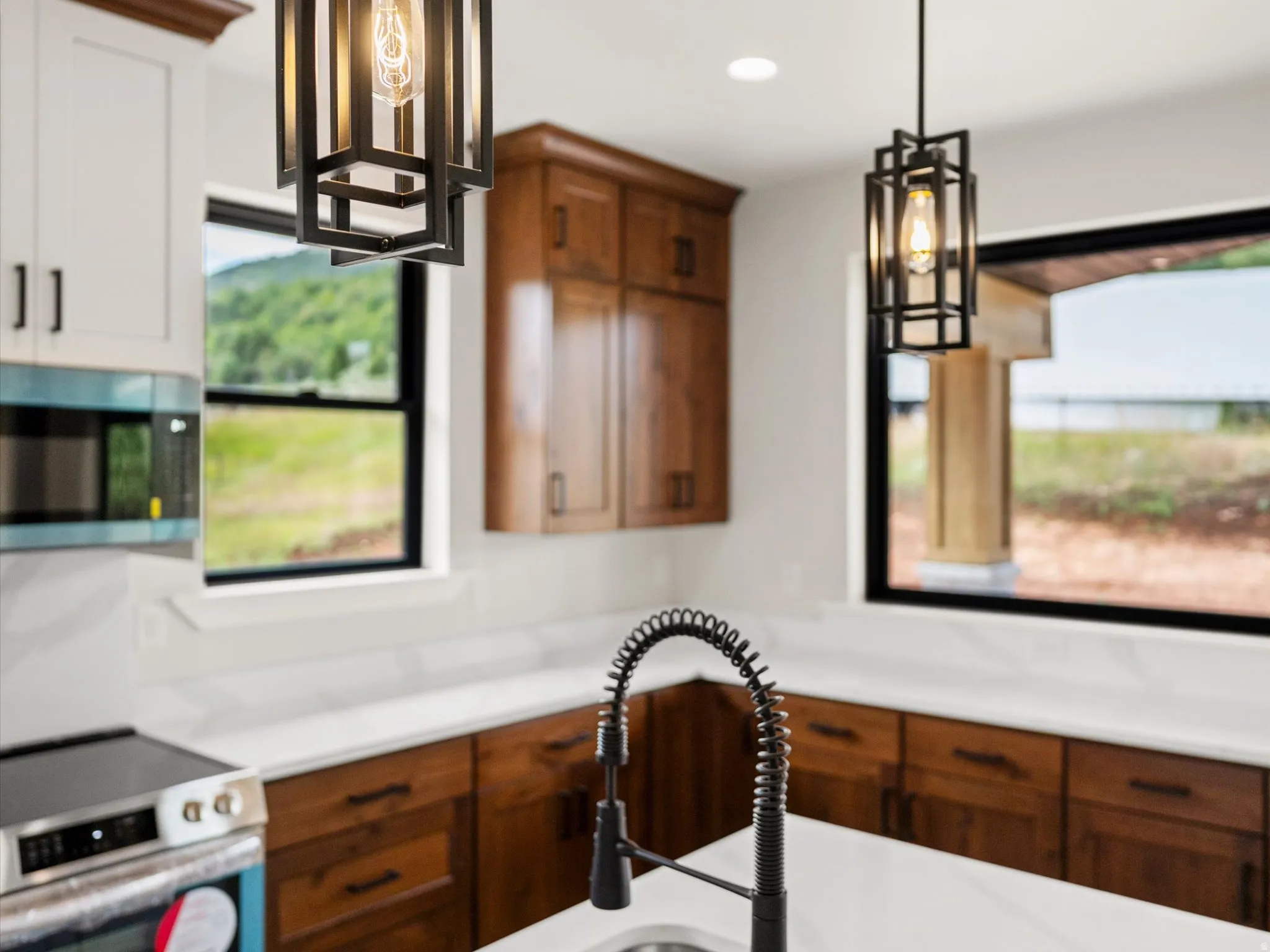 Kitchen featuring mixed-tone cabinetry, white countertops, stainless steel appliances, and two contemporary pendant lights