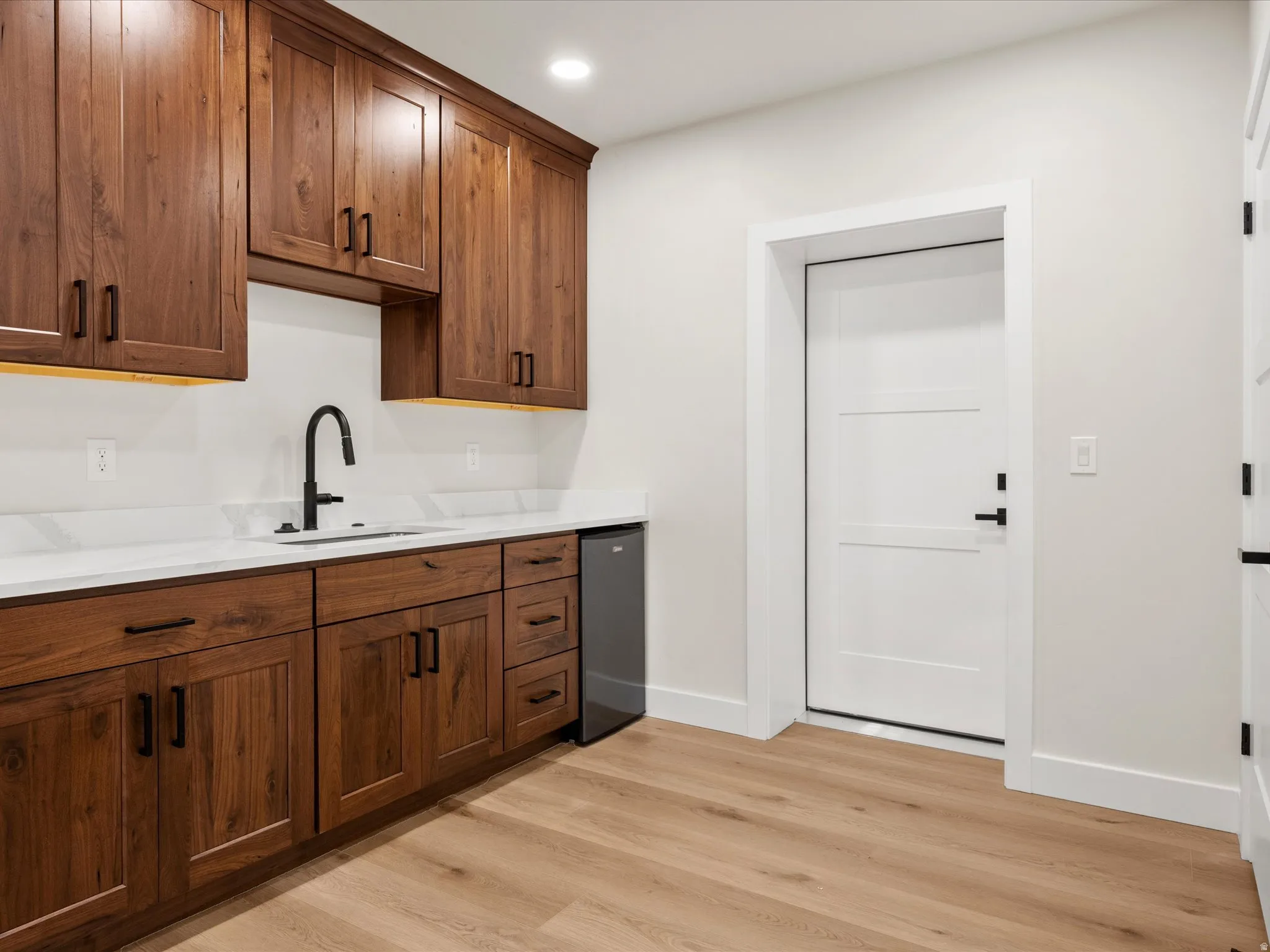 Wet bar featuring wood-finish cabinetry, white countertops, and a built-in beverage refrigerator