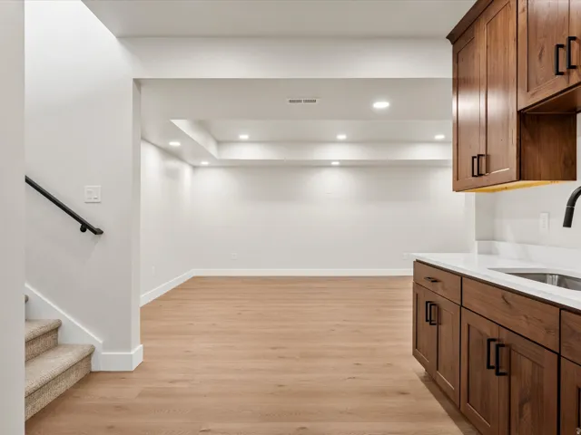 Finished lower level featuring recessed lighting, wood-finish flooring, and a wet bar with dark wood cabinetry, white countertop, and a matte black faucet