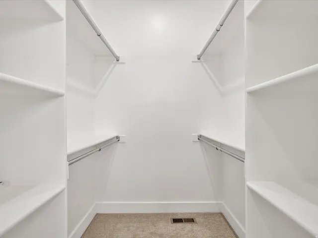 Walk-in closet featuring white built-in shelving, chrome hanging rods, and neutral-tone carpet flooring