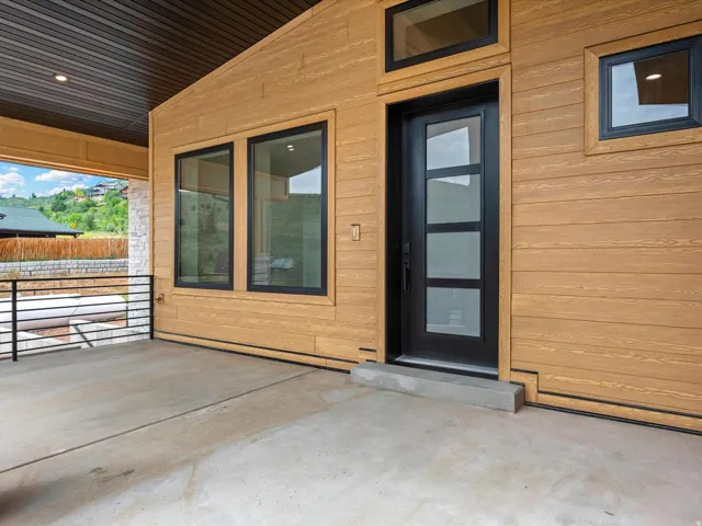 Modern entry featuring a dark-framed door with multiple glass panels, complemented by wood-finish siding and black-framed windows