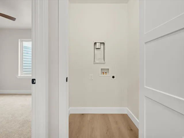 Dedicated laundry alcove featuring light wood-finish flooring, white baseboards, and neutral wall paint