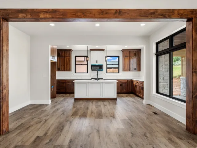 Expansive kitchen featuring a central island with integrated sink, recessed lighting, wood-finish flooring, two-tone cabinetry, and a large window with black framing
