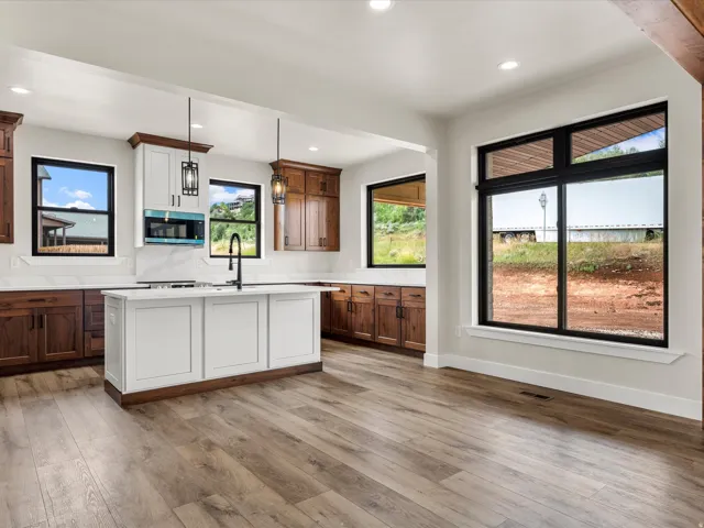 Spacious kitchen featuring a central island with paneling, wood-finish flooring, two-tone cabinetry, white countertops, and expansive windows with black framing