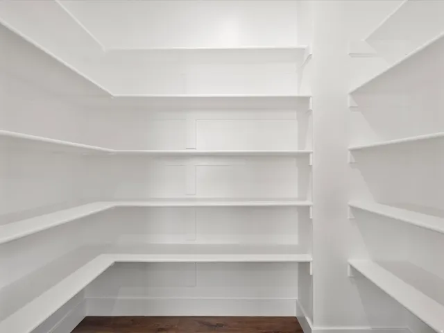 Walk-in pantry featuring white shelving, ample storage space, and dark wood-finish flooring