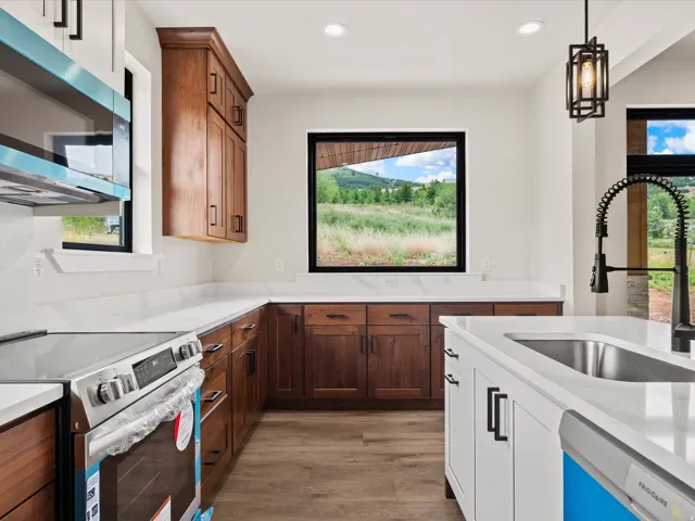 Kitchen featuring wood-finish lower and upper cabinetry, white countertops, built-in stainless steel appliances, and a kitchen island with an undermount sink and black pull-down faucet