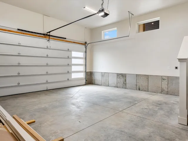 Spacious garage featuring a concrete floor, overhead door with frosted glass panels, automatic garage door opener, and two high-set windows