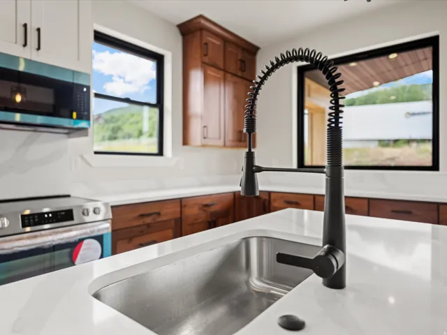 Stainless steel single basin sink with a matte black pull-down faucet, set into a white countertop