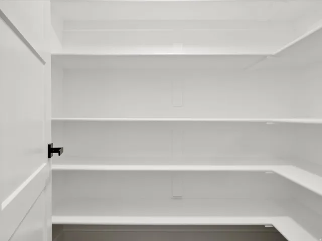 Pantry with multiple white shelves, a white interior, and a white door with a black handle