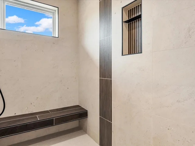 Shower enclosure featuring light-toned large format wall tiles, a built-in dark wood-finish bench, and a rectangular window